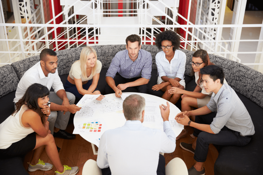 a group of people sitting around a sofa and table at an office at a fintech recruitment company